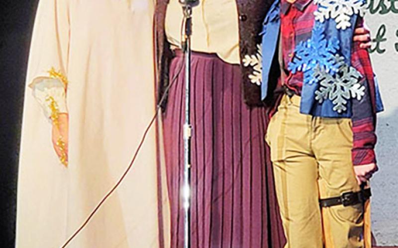 Bobbie Jo Cratchit, (with her children, Jane and Tim, by her side)  builds the courage to sing “God Bless Us Every One” for the Marley County talent contest on live radio.  Pictured from left: Jane Cratchit, played by Willow Williams, Bobbie Jo Cratchit, played by Bethany Beckett English, and Tim Cratchit, played by Carson Kelsch.