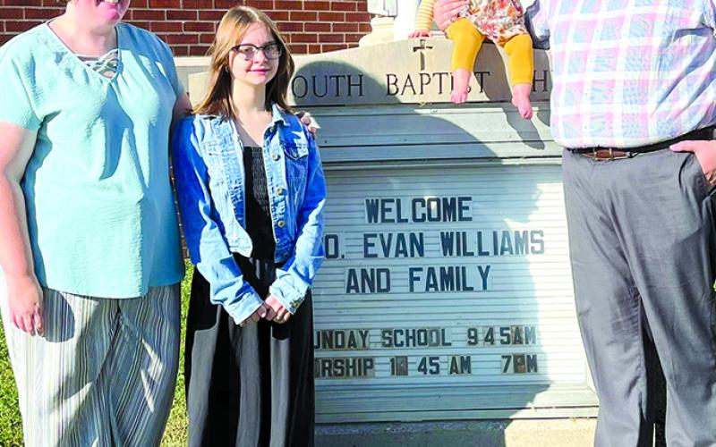 The Williams family stands around the sign that welcomes them. They are now in ministry at Falmouth Baptist Church.