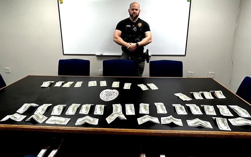 Officer Brody Schmeng stands by the table displaying the money that was secured from the subject as he was brought into the station after a domestic violence call.