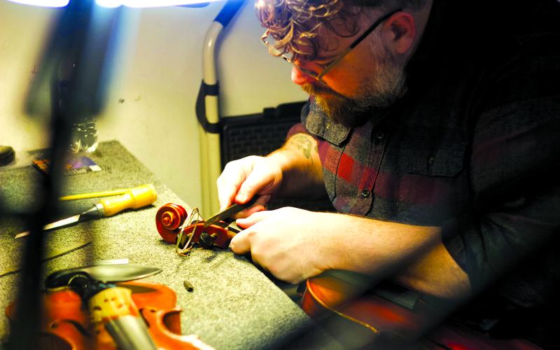 2005 Pendleton County High School graduate Brandon Godman repairs a violin in his shop, The Fiddle Mercantile, in San Francisco. Both a businessman and a recording artist who splits his time between San Francisco and Nashville, Godman said his latest solo album, “I Heard the Morgan Bell,” is his tribute to “back home.” Photo provided by Brandon Godman.