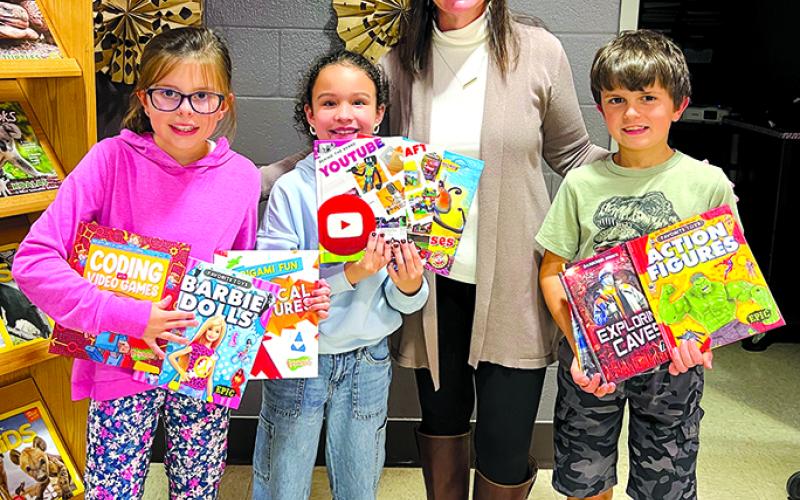 Northern Elementary School third-graders Lucy McCain, Monroe Johnson, media specialist Tina Record, and Jacob Hegyi show off some of the 100 books donated to the school by the newly opened Dollar General store in Butler. Photo by Nila Harris.