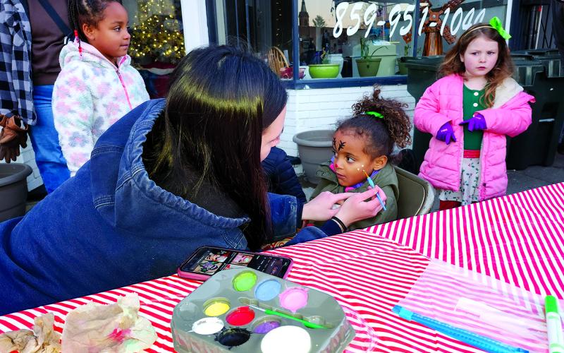 Kenzie Schmidt, left, paints a reindeer face on Cora Long, 3, while they wait for the parade. Cora, of Alexandria, was visiting her grandparents in Butler with her siblings when they all came out for the parade and festival on Shelby Street in downtown Falmouth. The face painting table was sponsored by Kincaid Lake State Park.