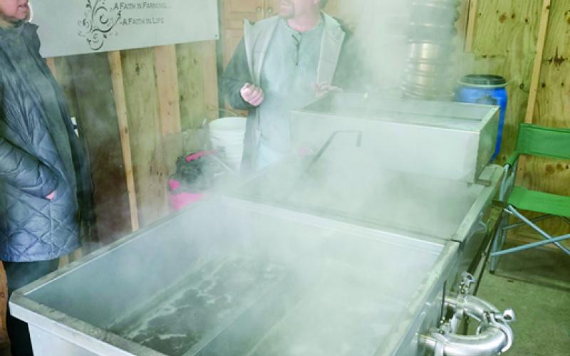 Jeff Pettit, center, is seen through the steam rising from the evaporator in his sugar shack at Faith Acres Farm in Butler as he explains the process of boiling sap from maple trees down to the syrup that goes so well on pancakes. Photo by Burton Cole.