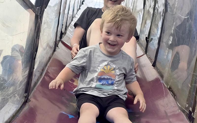 Jaxon Johnson, 2, and Isaac Mardis, 13, both of Butler, zip down the slide at the carnival portion of the fair. Photo by Jenny Smith.