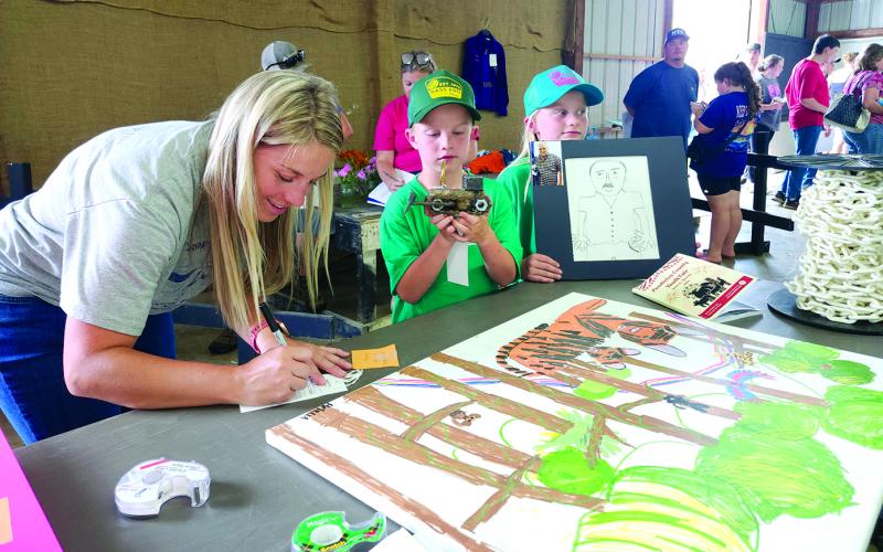 Mom Caitlin Ramsey of Falmouth, left, fills out the entry forms Sunday afternoon at the Pendleton County Youth Fair for the art projects created by her twins, Briella and Bohan Ramsey, 8, who are 4-H Cloverbuds. Bohan, center, holds a bulldozer that he welded from various scrap metal pieces including disc blades, bicycle chains, Allen wrenches and drill bits. Briella holds a sketch that she drew of her Papaw Curtis. One of her paintings is on the table. Fair set-up and exhibit registration was Sunday.