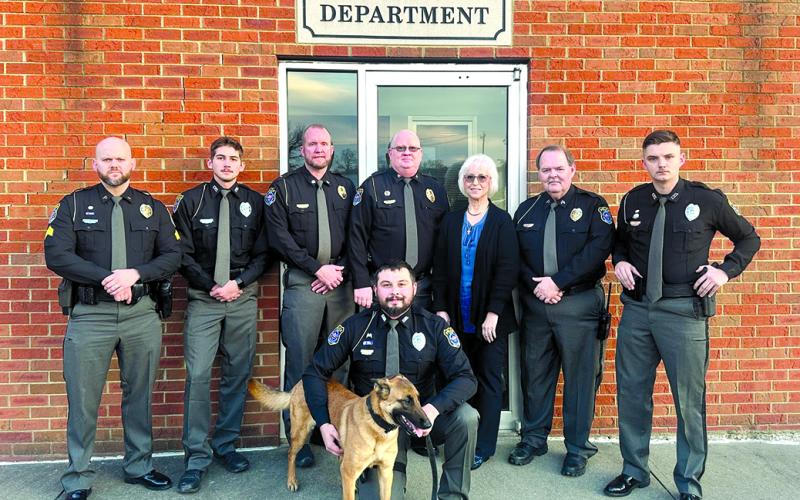 The Falmouth Police Department is, back row from left, Sgt. Broderick Schmeing, Officer Jonathon Bayless, Assistant Chief Nicholas Timon, Chief Marty Hart, office manager Marilyn Belcher, Sgt. Ken Hall and Officer Matthew Campbell. Kneeling is former K-9 Officer Kyle Florer with Cairo.