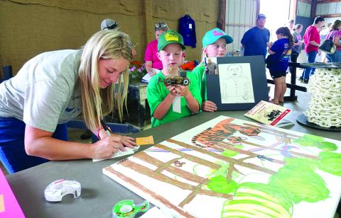 Mom Caitlin Ramsey of Falmouth, left, fills out the entry forms Sunday afternoon at the Pendleton County Youth Fair for the art projects created by her twins, Briella and Bohan Ramsey, 8, who are 4-H Cloverbuds. Bohan, center, holds a bulldozer that he welded from various scrap metal pieces including disc blades, bicycle chains, Allen wrenches and drill bits. Briella holds a sketch that she drew of her Papaw Curtis. One of her paintings is on the table. Fair set-up and exhibit registration was Sunday. 