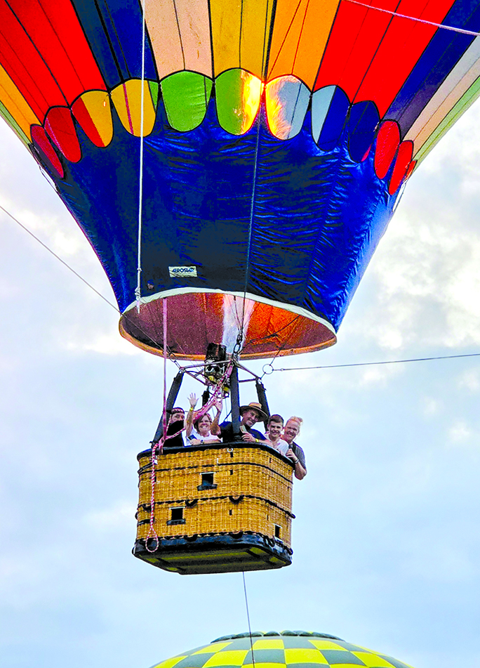Passengers suspended above the Wool Festival Grounds wave at people below. The passengers with the balloonist are Angie and Donnie Henry of California, Kentucky, and Tami Rehkamp and her son, Ethan, of Florence.