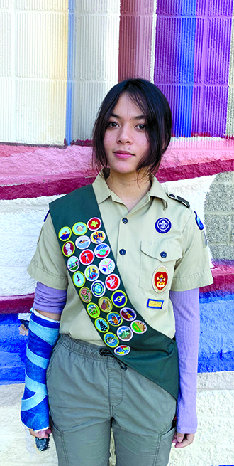 Crawford stands in her Scouting America uniform, a sash displaying badges she has earned. 