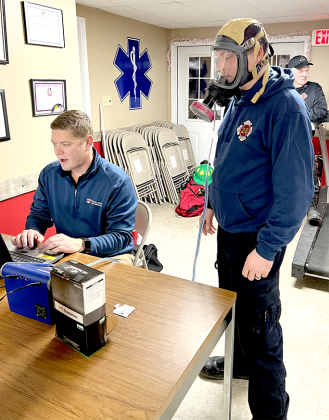 NPFD volunteer firefighter Josh Seitz gets fitted for a mask while sales representative Adam Bowsher inputs information into a database and makes adjustments.