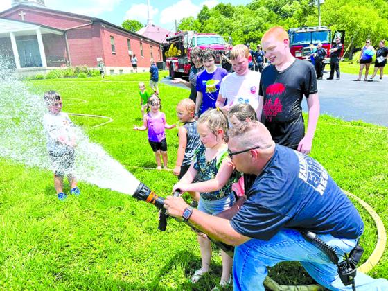 Asst. Fire Chief Travis Reis allows children to help with the hose as others have fun in the spray.