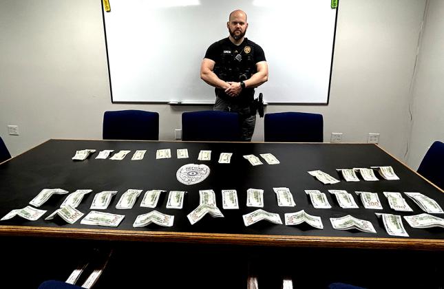 Officer Brody Schmeng stands by the table displaying the money that was secured from the subject as he was brought into the station after a domestic violence call.