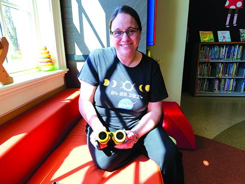 Pendleton County Public Library Programming Assistant Hannah Pearson holds a pair of Sunoculars, which appear to have black lenses. They are heavily filtered to allow the person using them to look directly at the sun. Photo by Burton Cole.