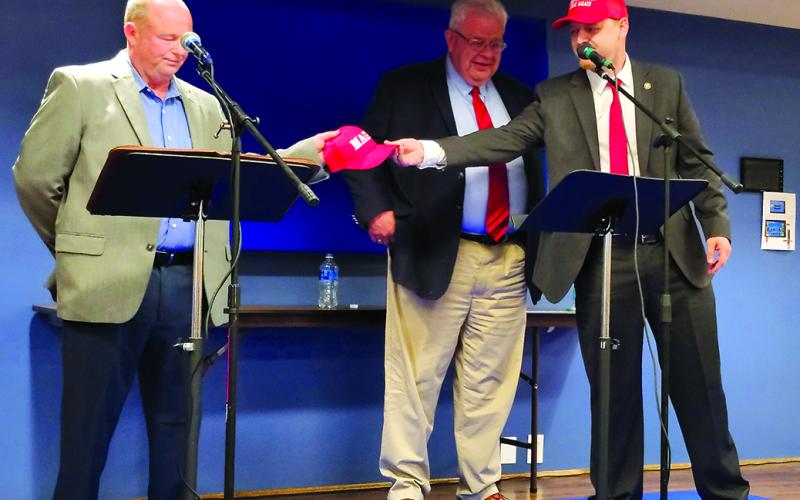 Enjoying a jab at the former registered Democrats, Sebastian Ernst hands MAGA caps to Rick Mineer, left, and Anthony Strong, welcoming them to the Republican Party. Photo by Burton Cole.